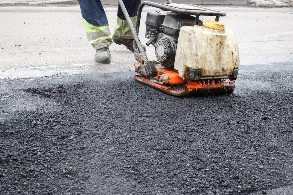 Close-up of worker using machine to press down fresh asphalt on road.
